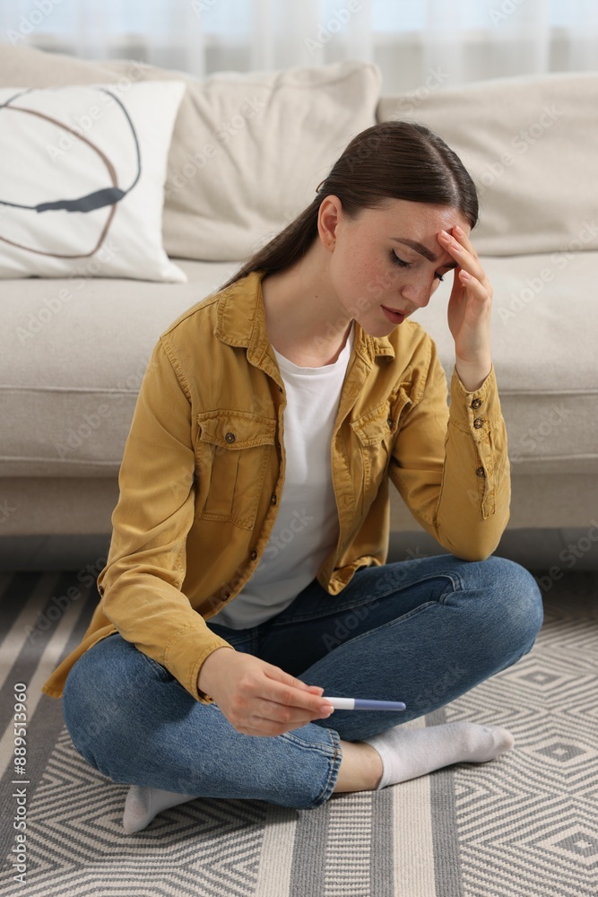 Obraz premium Sad woman holding pregnancy test on floor indoors