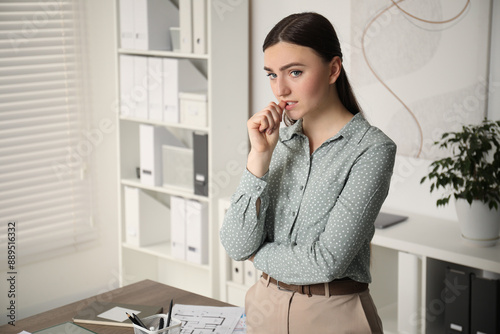 Embarrassed woman near table in office, space for text
