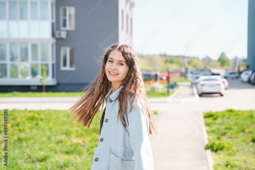 A young teenage girl walks along an empty street between high-rise buildings. Teenage high school student girl with backpack on city street