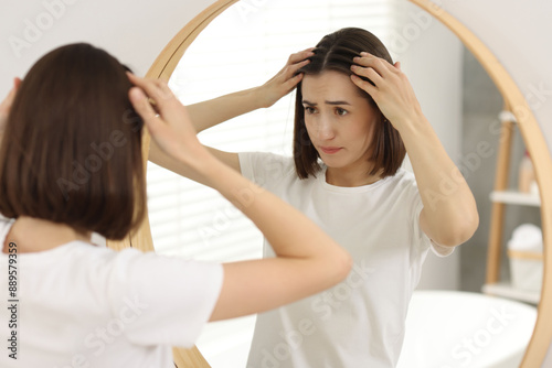 Sad woman with hair loss problem looking at mirror indoors