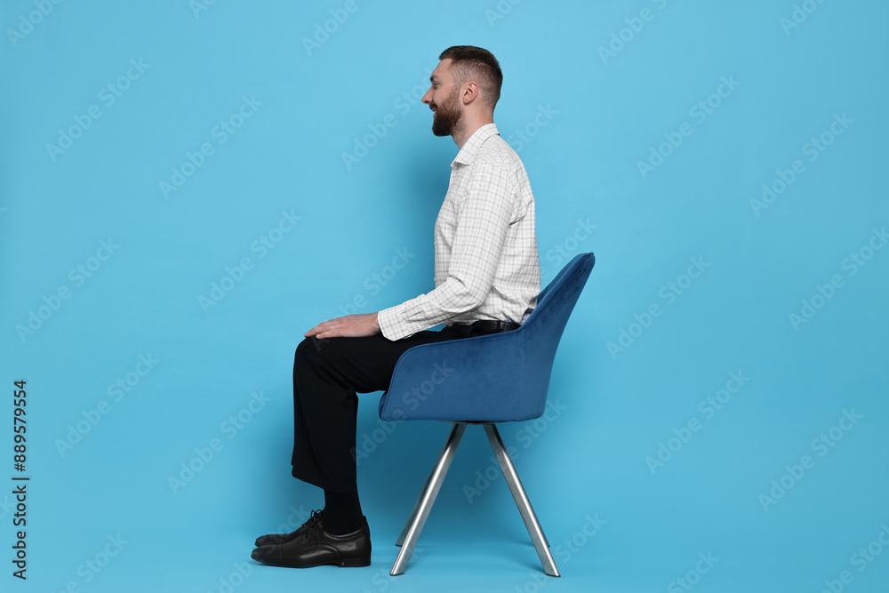 Man with good posture sitting on chair against light blue background Man with good posture sitting on chair against light blue background