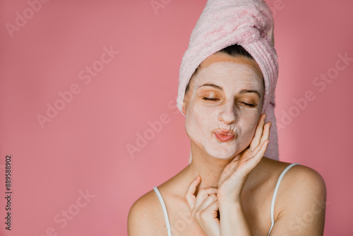 A beautiful young woman in towel in a facemask blows a kiss in her bathroom while doing her facecare morning routine 
