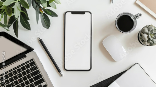 A white iPhone sits on a desk next to a laptop and a mouse
