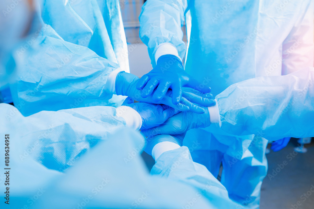 Closeup medical team in blue uniforms and gloves join hands, symbolizing teamwork and unity in healthcare preparation with sunlight. Closeup medical team in blue uniforms and gloves join hands, symbolizing teamwork and unity in healthcare preparation with sunlight.