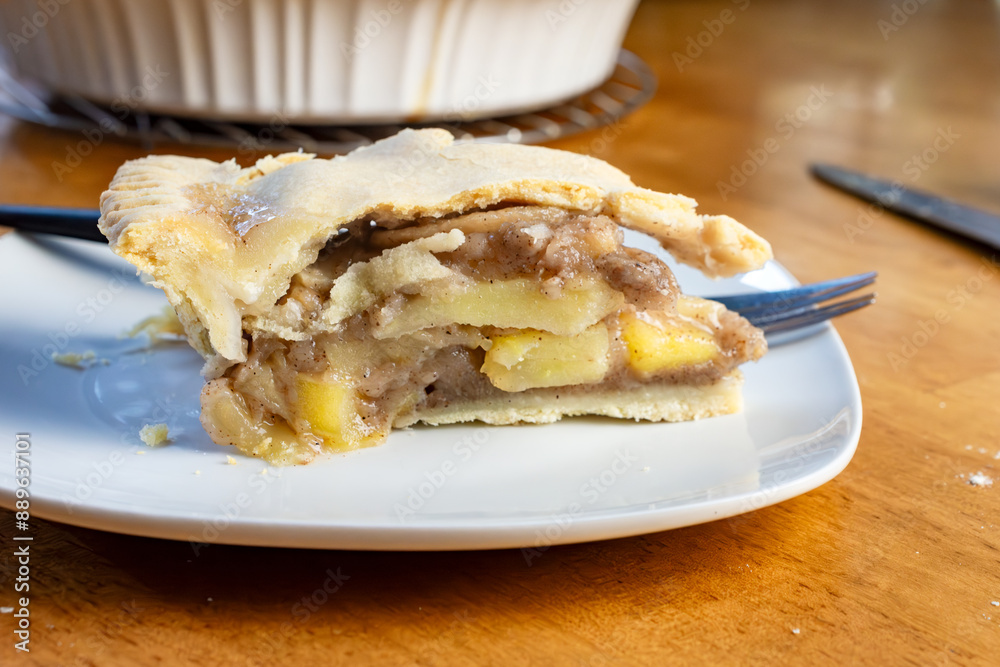 A slice of apple pie sits on a wooden table with a black handled fork. A slice of apple pie sits on a wooden table with a black handled fork.