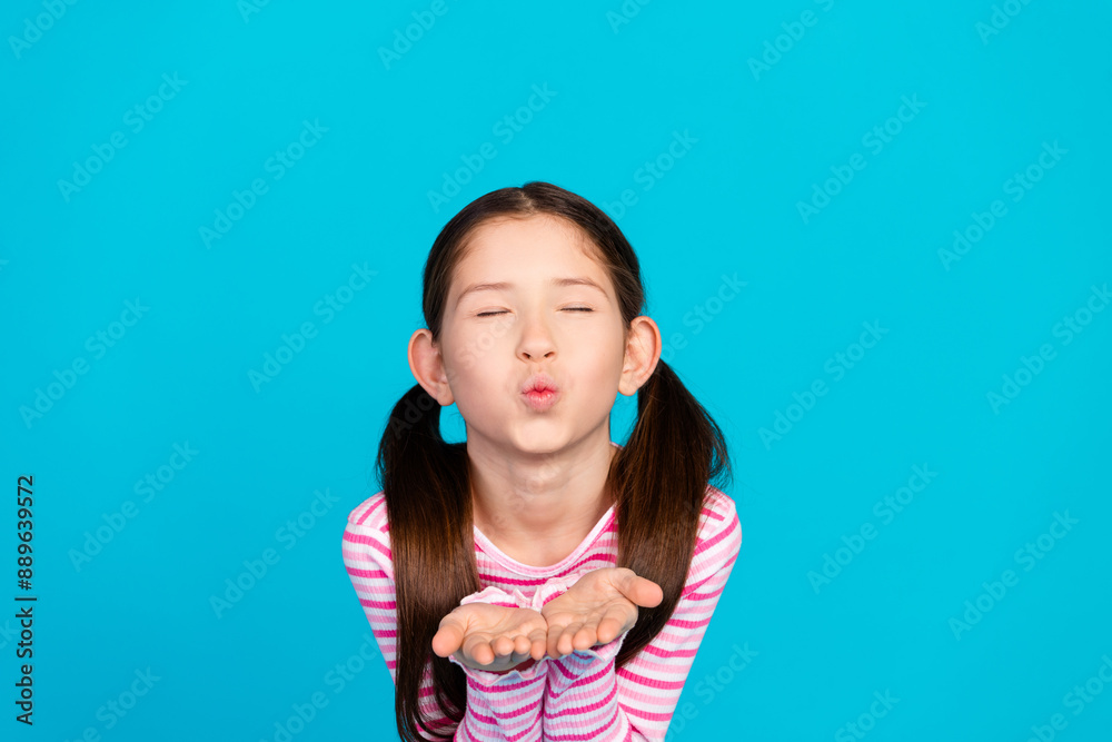 Photo of adorable positive small girl with ponytails dressed striped shirt send air kiss close eyes isolated on blue color background Photo of adorable positive small girl with ponytails dressed striped shirt send air kiss close eyes isolated on blue color background