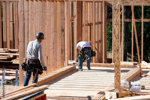 Construction work crew building a new house in a residential neighborhood, wood framing started, sunny summer construction season
