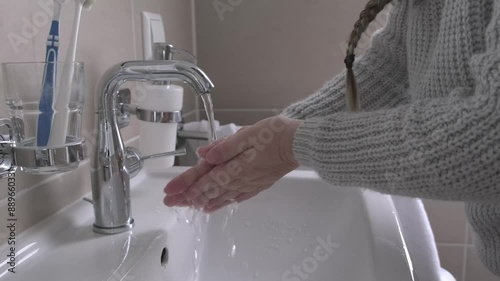 middle-aged woman washing hands in bathroom basin, highlighting importance of good hygiene and self-care for healthy lifestyle