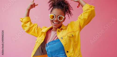 Smiling Woman Wearing a Yellow Jacket and Sunglasses Posing on Pink Background
