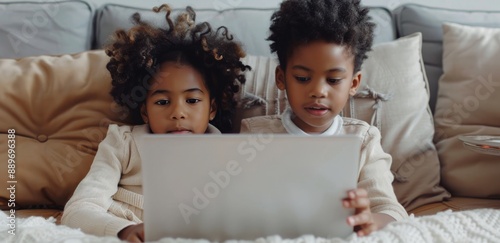 Two Young Children Using Laptops On A Grey Couch