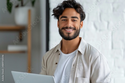 A man with a beard and a white shirt is smiling and holding a laptop. Concept of happiness and productivity, as the man is working or studying while enjoying his time