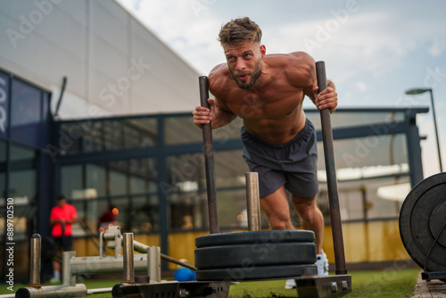 Muscular caucasian fitness instructor pushing a weighted sled during an outdoor workout at a gym. photo