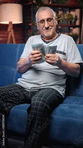 Rich old man accounting his money, holding cash dollars in hands, sitting in apartment, portrait