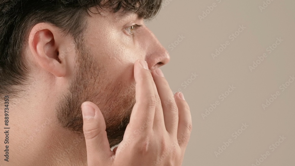 Young adult man looking at camera female applies cream on his face, isolated on white background. Natural beauty skin care concept. Side view. Young adult man looking at camera female applies cream on his face, isolated on white background. Natural beauty skin care concept. Side view.