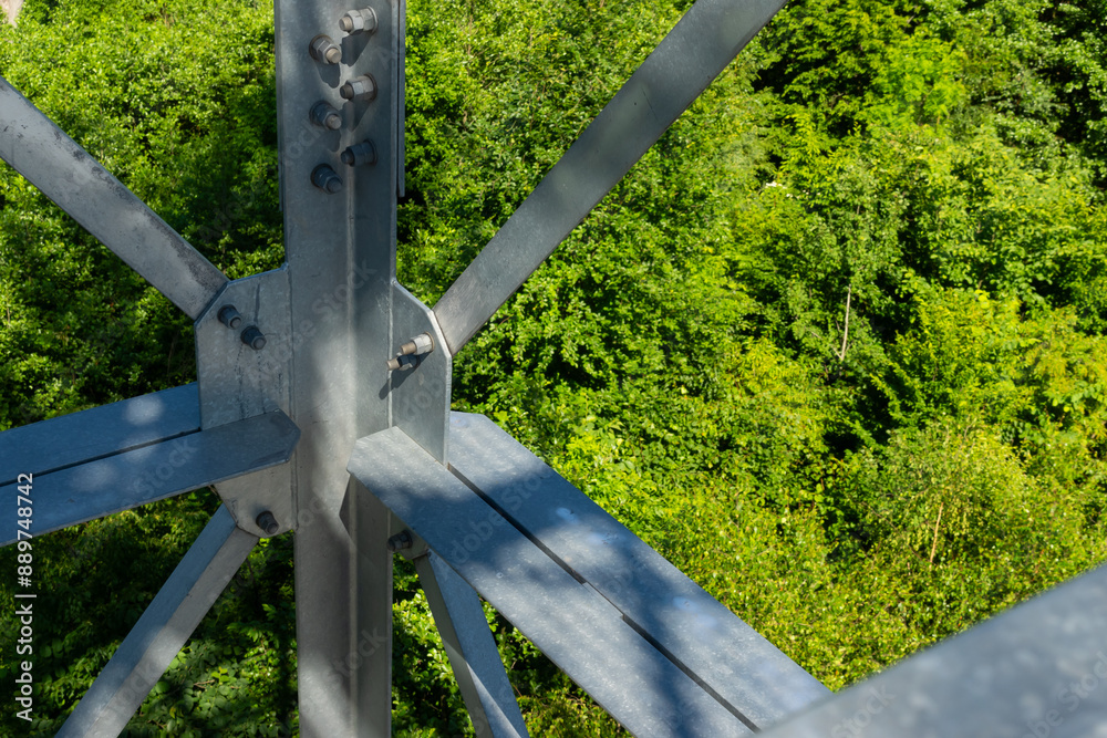 Bolted connections of steel elements of the observation tower. Construction details of galvanized steel against a green trees background