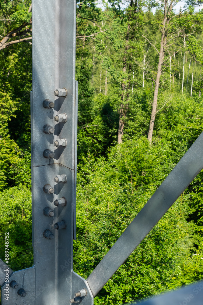 Bolted connections of steel elements of the observation tower. Construction details of galvanized steel against a green trees background