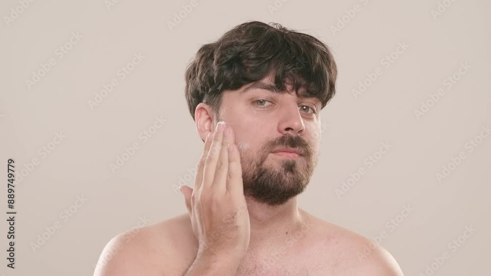 Young adult man applies aftershave cream moisturizer looks at camera, isolated on white background. Natural beauty skin care concept Young adult man applies aftershave cream moisturizer looks at camera, isolated on white background. Natural beauty skin care concept