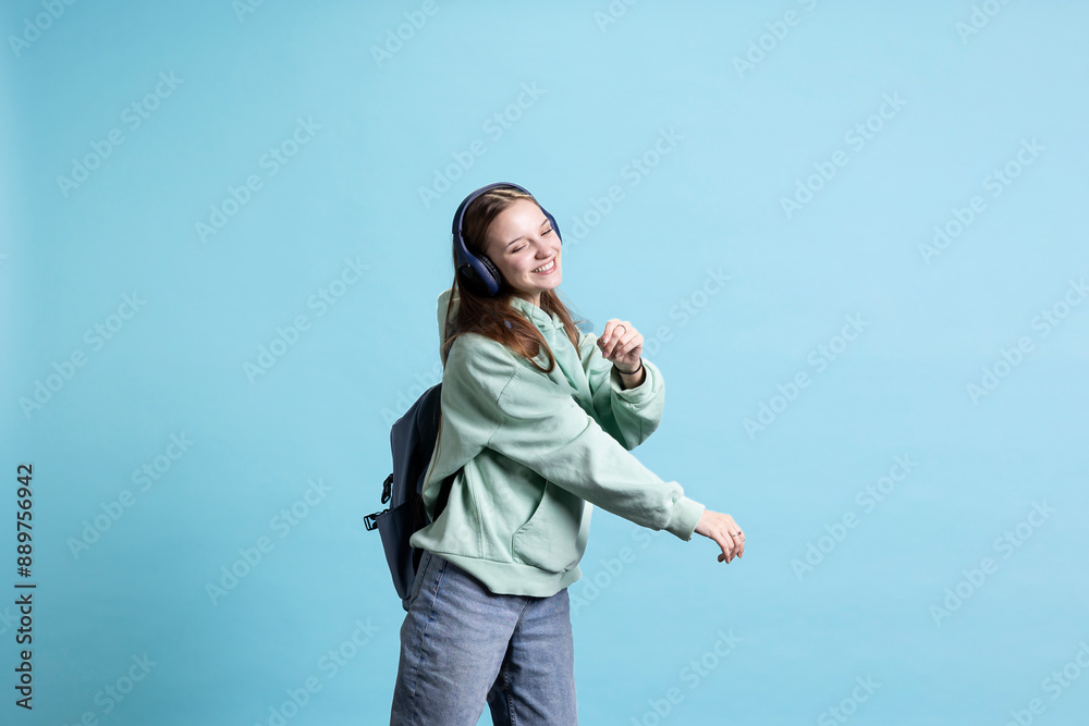 Jolly teenager enjoying music, dancing with headphones, having expressive body language. Cheerful young girl wearing headset, having fun on funky rhythm songs, isolated over studio background