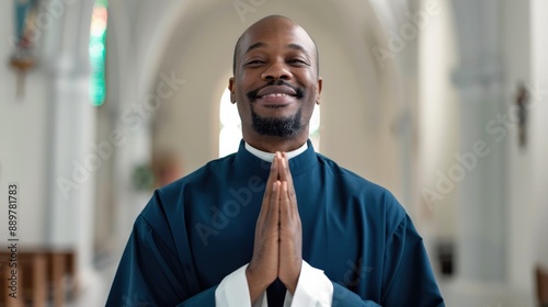 Smiling clergyman in a blue robe praying with hands together in a beautifully lit church, radiating peace and devotion. photo