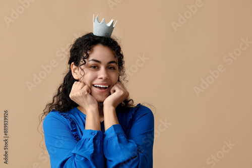 Beautiful young African-American woman in paper crown on brown background photo