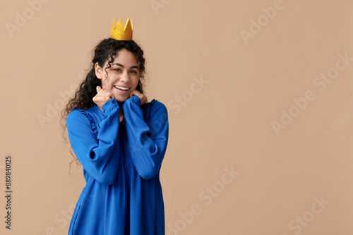 Happy young African-American woman in paper crown on brown background photo