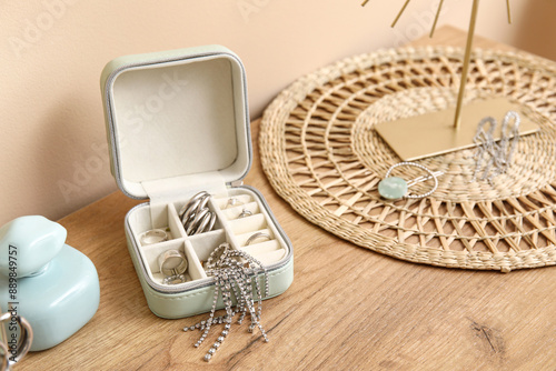 Box with stylish different jewelry and perfume bottle on dresser near beige wall