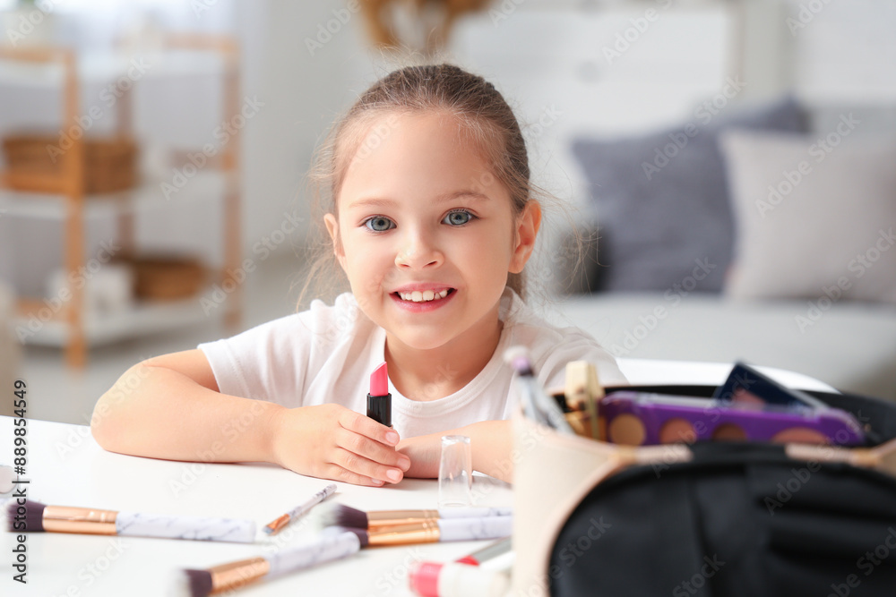 Cute little girl with lipstick and makeup brushes at table in living room Cute little girl with lipstick and makeup brushes at table in living room