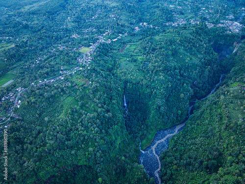 Aerial view Kabut Pelangi Waterfall in East Java. The waterfall stream flows into the mountain gorge in a long path.Above is the residence of the villagers. Abundance of forests on the green mountain. photo