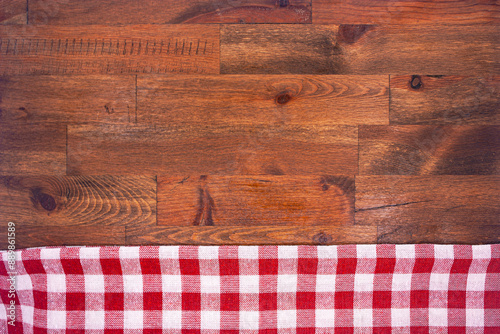 Red and white checkered, plaid tablecloth on wooden surface. Top view. Photograph.