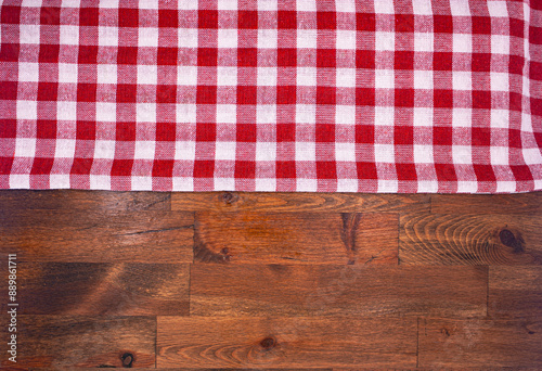 Red and white checkered, plaid tablecloth on wooden surface. Top view. Photograph.