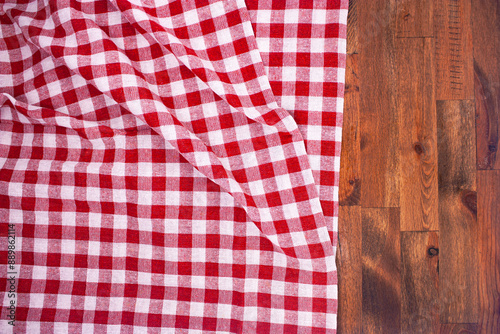 Red and white checkered, plaid tablecloth on wooden surface. Top view. Photograph.