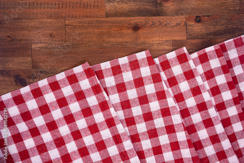 Red and white checkered, plaid tablecloth on wooden surface. Top view. Photograph.