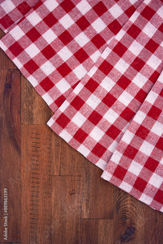 Red and white checkered, plaid tablecloth on wooden surface. Top view. Photograph.