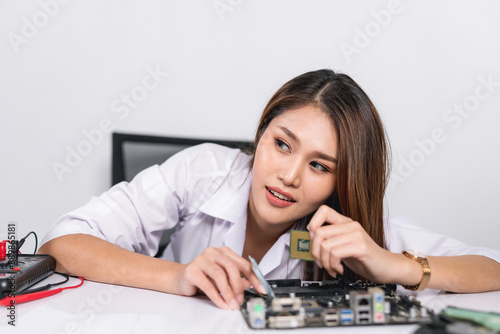 Beautiful young woman repairing electronic circuit board or computer parts on her table. Service center. Repair service. Gray background.