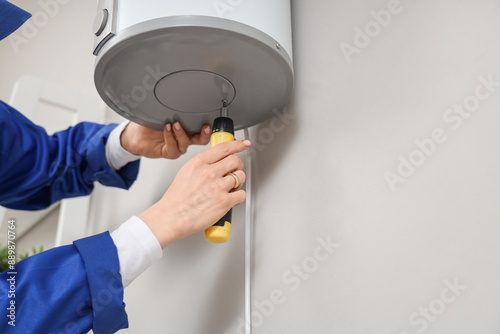 Фотография Female worker with screwdriver fixing modern electric boiler in bathroom