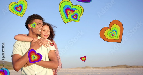 Image of hearts moving over diverse couple in love embracing on beach in summer