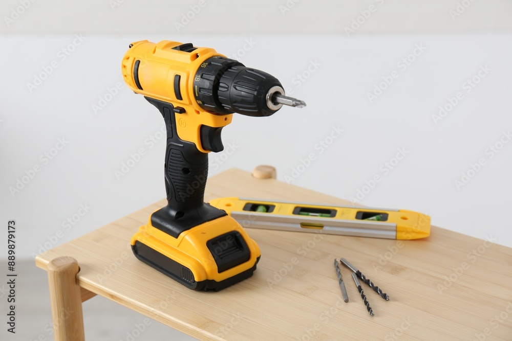 Electric screwdriver, drill bits and building level on wooden table against light background Electric screwdriver, drill bits and building level on wooden table against light background