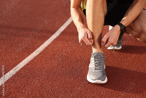 Man tying shoelace of grey sneaker at stadium, closeup. Space for text