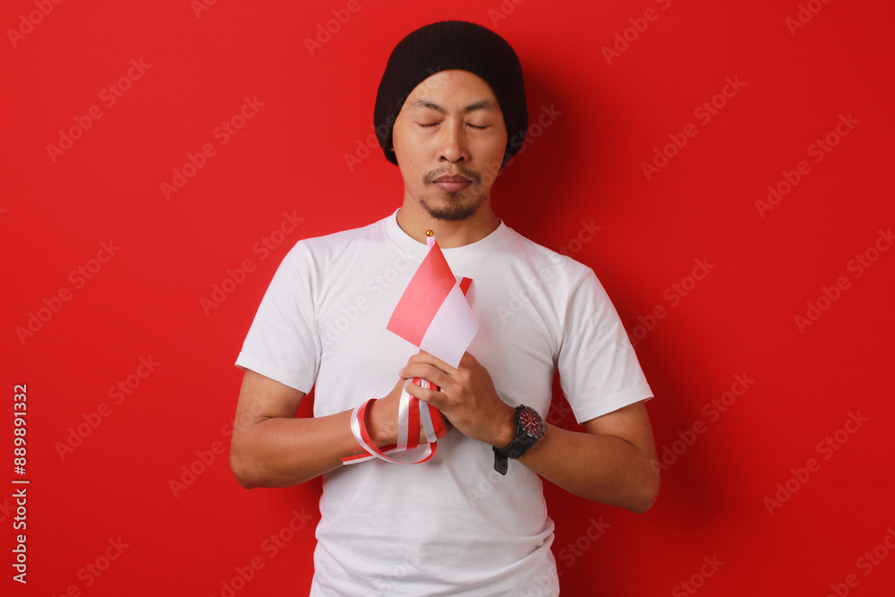 Indonesian youth holds a moment of silence while holding the Indonesian flag, remembering the struggle of the heroes who have fallen for Indonesia independence Day, isolated on a red background Indonesian youth holds a moment of silence while holding the Indonesian flag, remembering the struggle of the heroes who have fallen for Indonesia independence Day, isolated on a red background