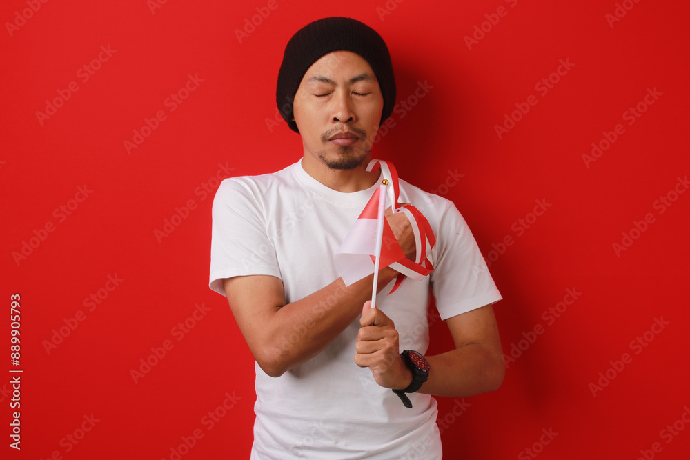 Indonesian youth holds a moment of silence while holding the Indonesian flag, remembering the struggle of the heroes who have fallen for Indonesia independence Day, isolated on a red background Indonesian youth holds a moment of silence while holding the Indonesian flag, remembering the struggle of the heroes who have fallen for Indonesia independence Day, isolated on a red background