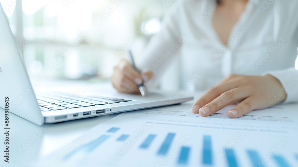 Business professional reviewing financial documents, analyzing data on laptop, working at desk in bright office environment