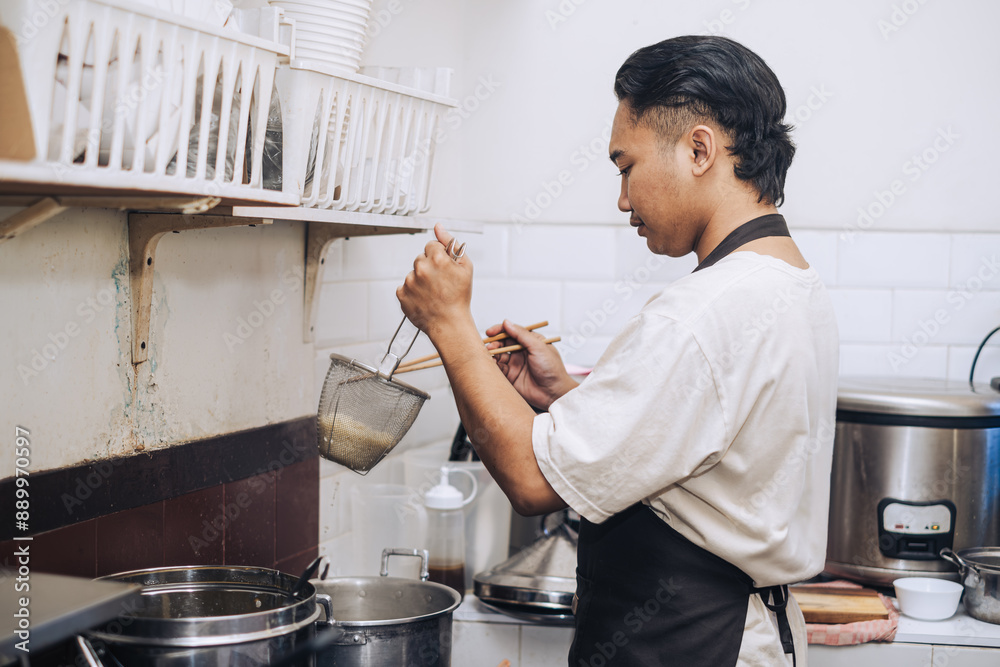 A Southeast Asian chef with an apron is cooking the noodles with bokeh background A Southeast Asian chef with an apron is cooking the noodles with bokeh background