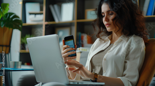 Businesswoman holding phone with text payment successful on screen display, sitting in office chair at desk or table with laptop notebook on workplace. Online internet shopping, purchase invoice