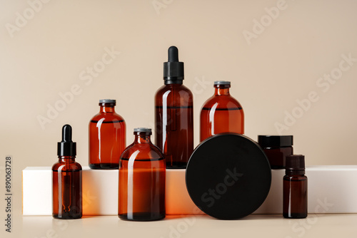 Set of brown glass bottles with essential oils on stand on beige background