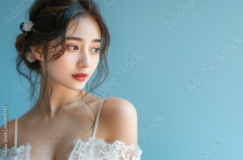 Beautiful Japanese girl wearing white dress with lace and shoulder straps on light blue background with copyspace best for makeup and cosmetics ads