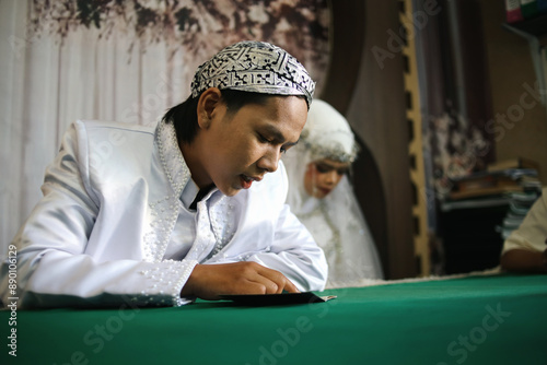 Young Asian Groom Reading Marriage Book With Bride Beside Him In Indonesian Wedding photo