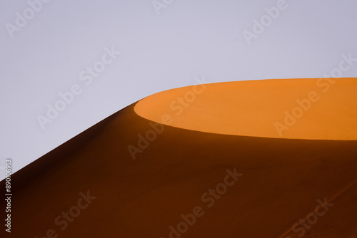 Fototapeta Naklejka Na Ścianę i Meble -  A sunlit sand dune stands out against a clear sky, capturing the minimalist beauty and striking contrasts of the Namibian desert landscape.