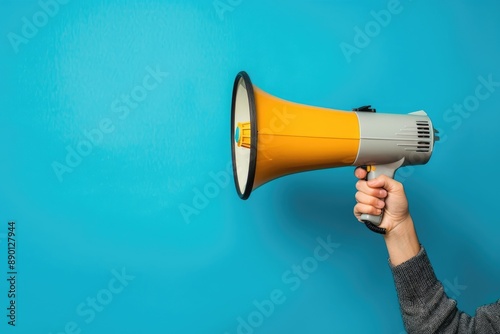 Hand holding a bright yellow megaphone against a blue background © MrHamster