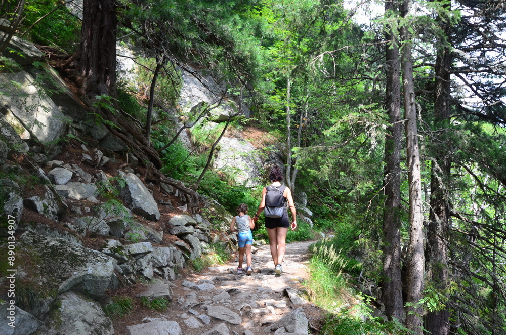 The picturesque landscape features towering peaks, lush alpine forests, and a clear blue summer sky with scattered clouds. In the distance, a family enjoys their outdoor adventure, The picturesque landscape features towering peaks, lush alpine forests, and a clear blue summer sky with scattered clouds. In the distance, a family enjoys their outdoor adventure,