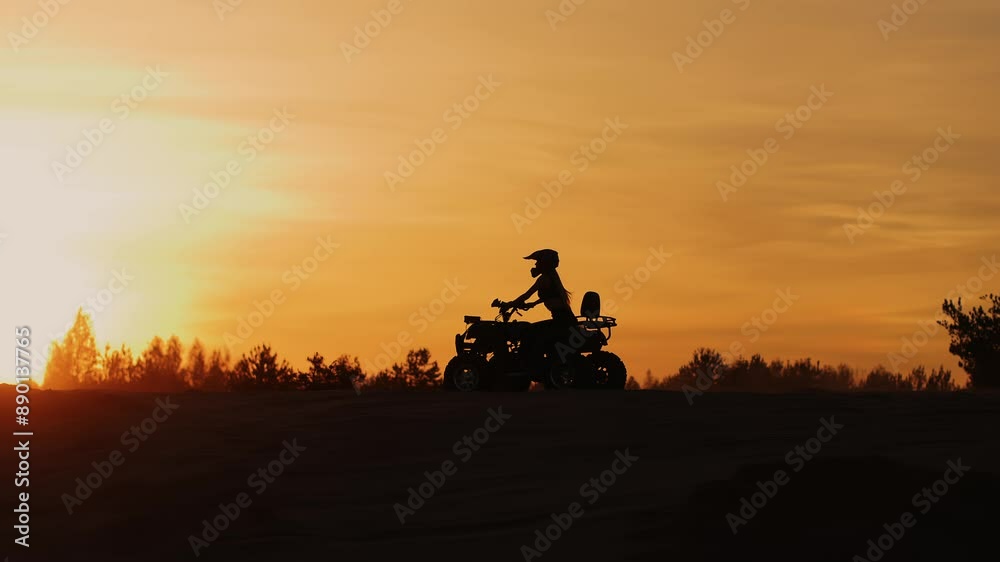 Young girl in helmet rides an quad bike along top of hill against backdrop of sunset. Slow motion. Cross country racing and mastering track Young girl in helmet rides an quad bike along top of hill against backdrop of sunset. Slow motion. Cross country racing and mastering track